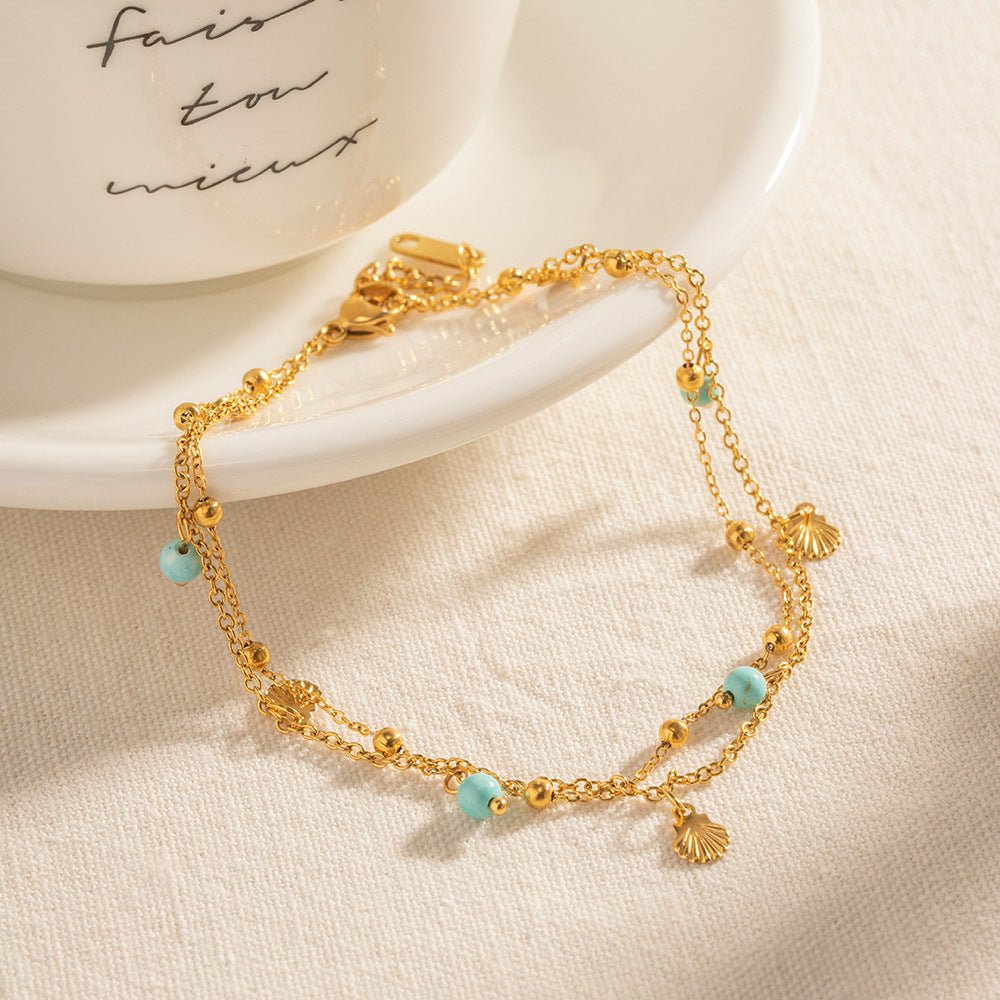 Bracelet de cheville double rang en acier doré avec perles turquoise et petit pendentif rond.