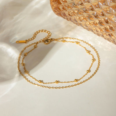 Bracelet de cheville double rang en acier inoxydable doré avec petites perles et chaîne fine.