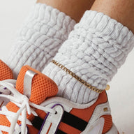 Bracelet de cheville maille cubaine en acier inoxydable or rosé porté avec chaussettes blanches et baskets orange.