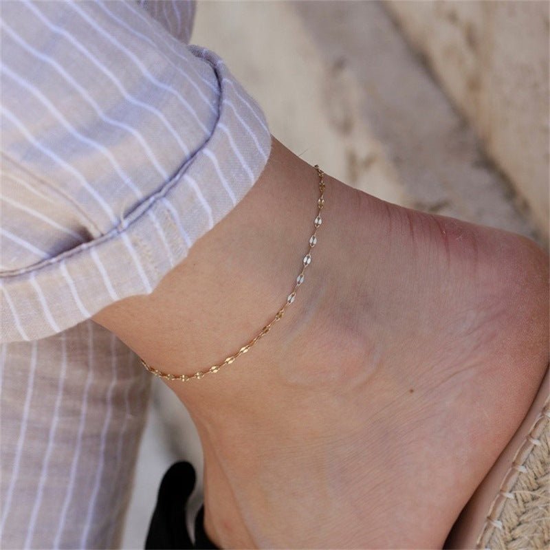 Bracelet de cheville en acier inoxydable argenté avec maille grain de café fine sur peau féminine.