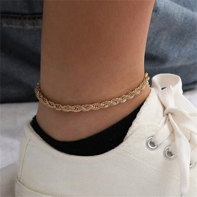 Bracelet de cheville en acier inoxydable doré, maille torsadée fine, porté avec baskets blanches.
