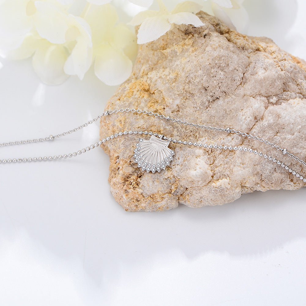 Bracelet de cheville en argent sterling avec pendentif coquillage fin posé sur pierre claire.