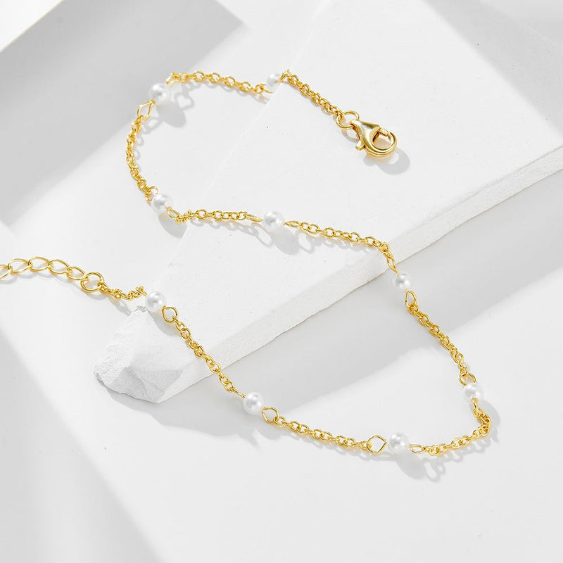 Bracelet de cheville en chaîne fine dorée avec petites perles d'eau douce blanches espacées régulièrement.