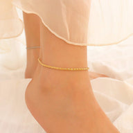 Bracelet de cheville en titane or à maille scintillante, modèle Lamina, porté sur peau pâle.