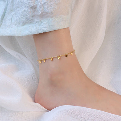 Bracelet de cheville en titane doré avec multiples petits médaillons ronds suspendus.