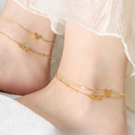 Bracelet de cheville en titane doré avec pendentifs cœur et inscription "love", style délicat et féminin.