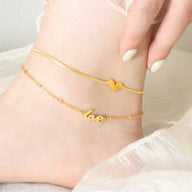 Bracelet de cheville doré en titane avec pendentif cœur et motif "love" délicat.