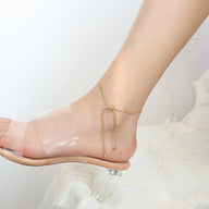 Bracelet de cheville coulissant en titane or, chaîne fine avec petits ornements ronds, porté avec sandale à bride.