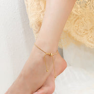 Bracelet de cheville coulissant en titane couleur or avec pendentifs ronds sur peau féminine.