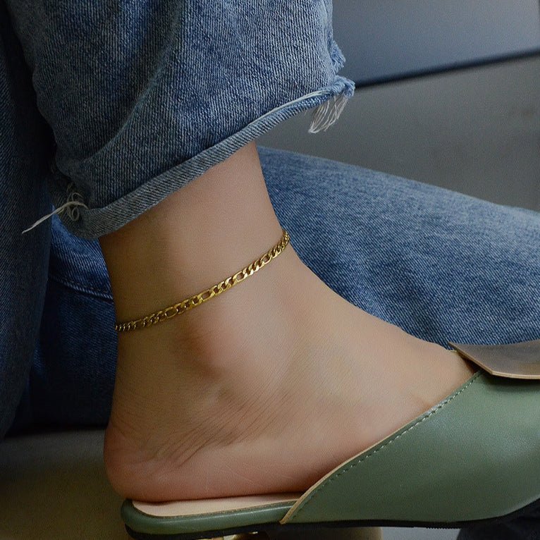 Bracelet de cheville en titane doré avec maille figaro fine, porté avec jean et mule verte.