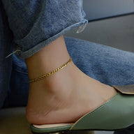 Bracelet de cheville en titane doré avec maille figaro fine, porté avec jean et mule verte.