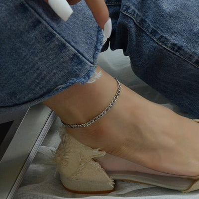 Bracelet de cheville en titane argenté à maille Figaro fine porté avec jean et escarpin beige.