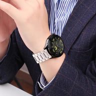 Bracelet de montre connecté Huawei en acier inoxydable argenté à maillons porté au poignet d'un homme en costume bleu.