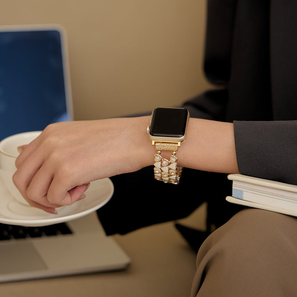 Bracelet Apple Watch or rosé à motif cœurs portés sur poignet féminin, style élégant et contemporain.