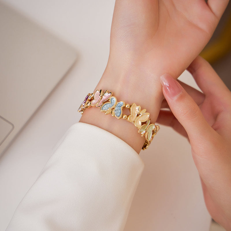 Bracelet pour Apple Watch à motif papillons multicolores sur fond doré porté au poignet féminin.