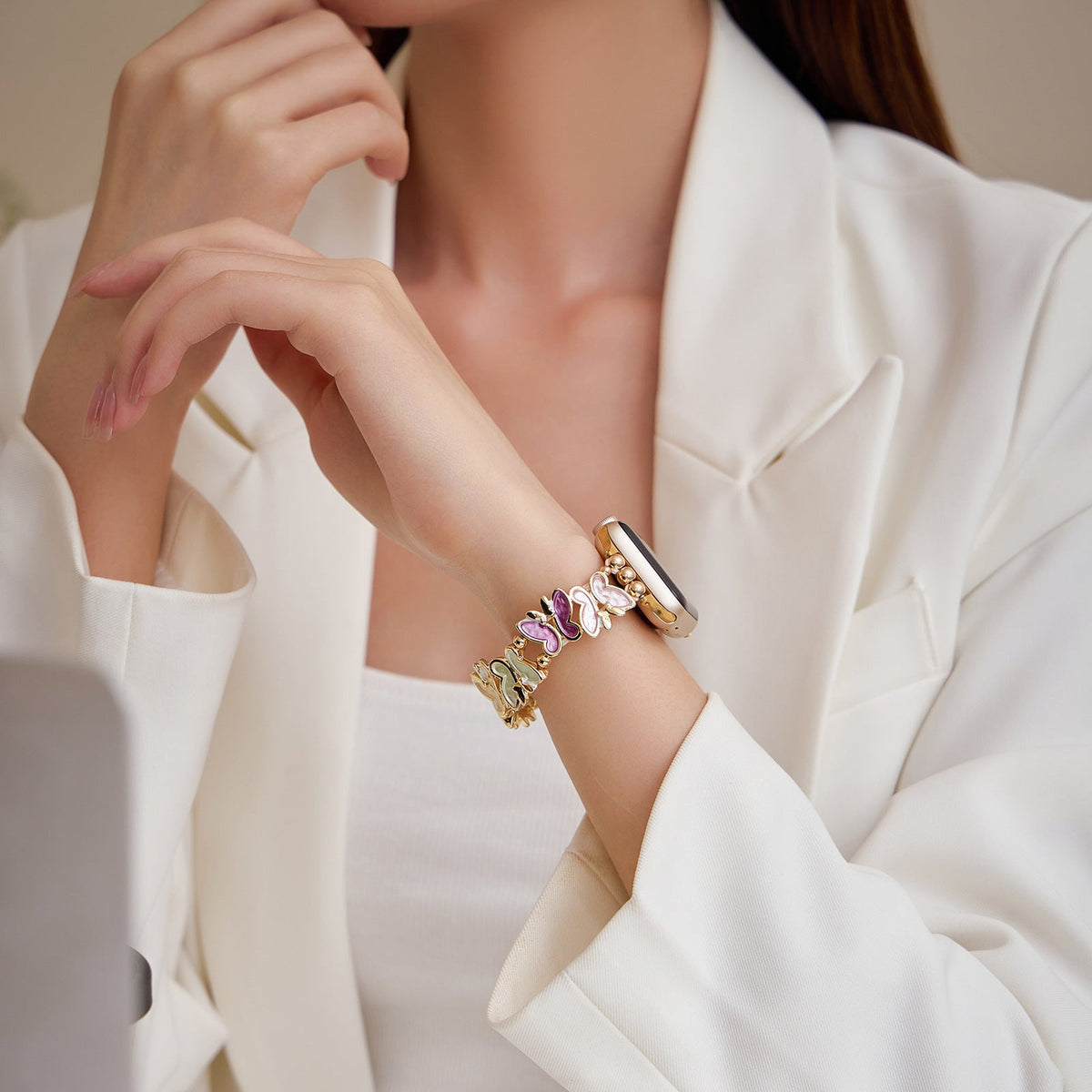 Bracelet Apple Watch or avec motifs papillons multicolores porté sur poignet féminin en veste blanche.