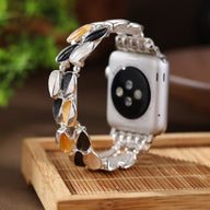 Bracelet Apple Watch femme en métal argenté avec pétales en noir, gris et doré scintillant.