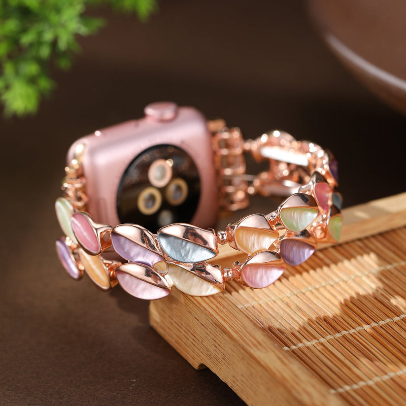 Bracelet Apple Watch femme en métal rose avec pétales scintillants multicolores et maillons élégants.