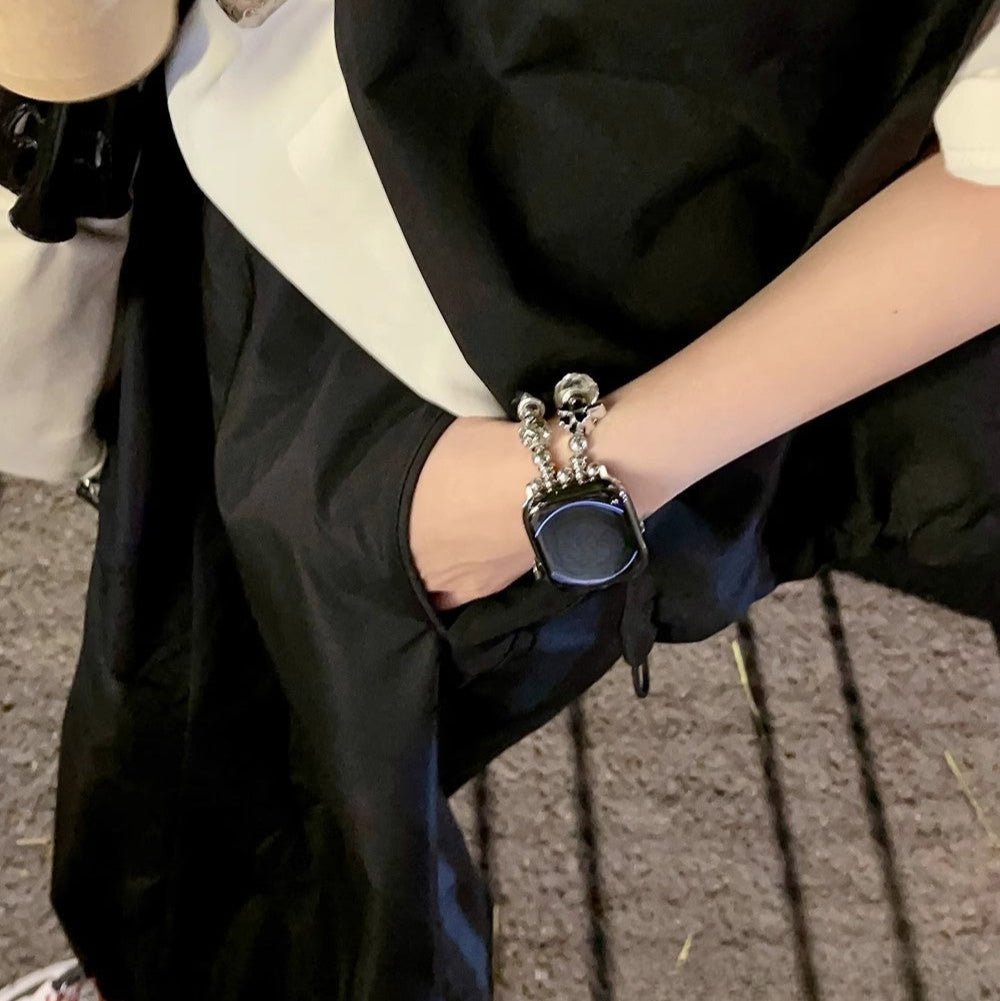 Bracelet Apple Watch double-rang noir avec multi-charms argentés porté au poignet femme.