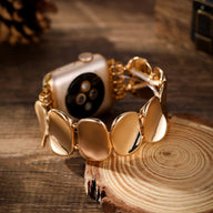 Bracelet en alliage métallique doré avec maillons larges et lisses pour Apple Watch sur fond bois naturel.