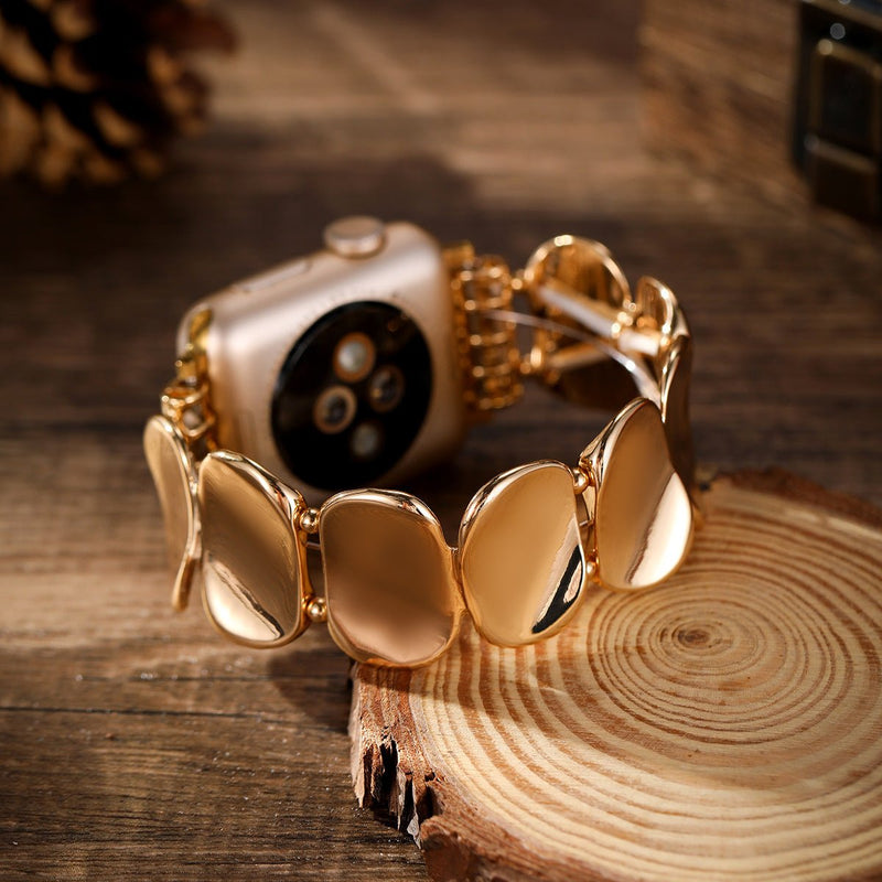 Bracelet en alliage métallique doré avec maillons larges et lisses pour Apple Watch sur fond bois naturel.