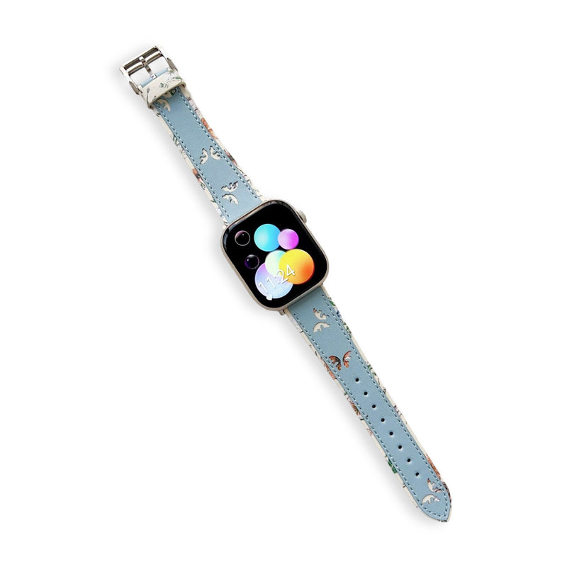Bracelet Apple Watch en cuir bleu ciel avec motif papillons blancs et boucle argentée.