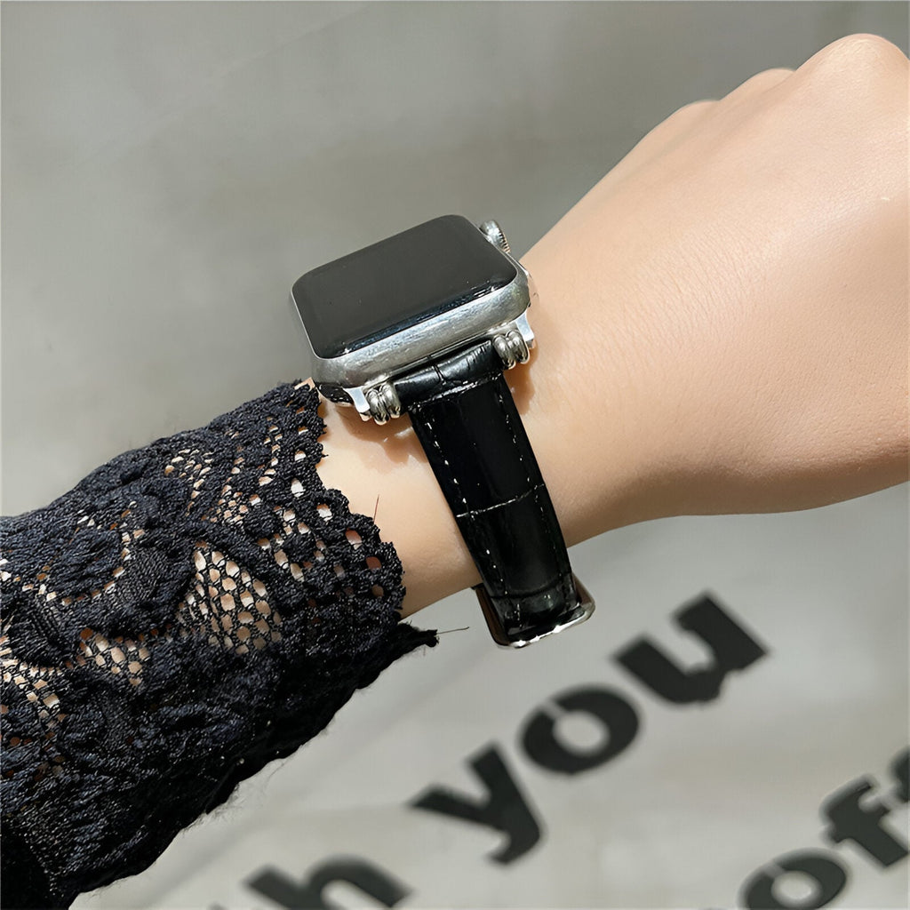Bracelet Apple Watch en microfibre noir à texture lisse avec boucle argentée sur poignet féminin.