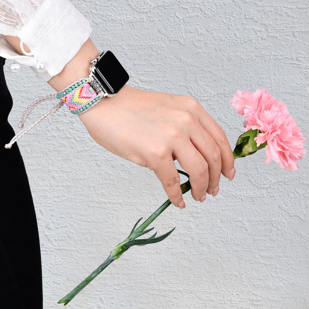 Bracelet Apple Watch en nylon rose avec cristaux multicolores, porté au poignet féminin, tenant une fleur rose.