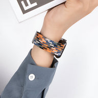 Bracelet Apple Watch en nylon tressé orange, noir et beige, fermé sur poignet avec chemise grise.
