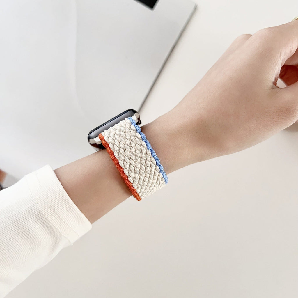 Bracelet Apple Watch nylon blanc avec bords orange et bleu porté au poignet femme.