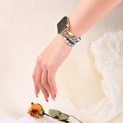 Bracelet Apple Watch multicolore en pierres de cristal brillantes porté sur poignet féminin avec robe blanche en tissu léger.