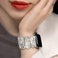 Bracelet Apple Watch en résine blanc tacheté motifs noirs, style large et arrondi, porté au poignet féminin.