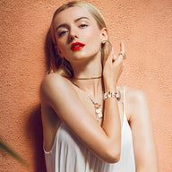 Bracelet Apple Watch en résine blanche avec motifs dorés portés au poignet d'une femme blonde au fond saumon.