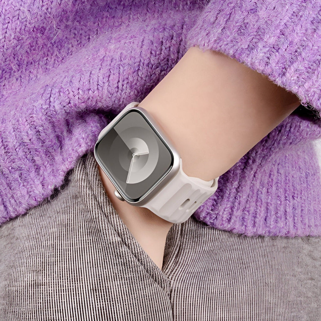 Bracelet Apple Watch en silicone beige clair porté avec un pull violet en laine côtelée.