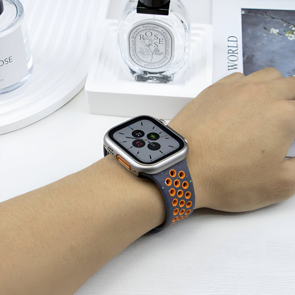 Bracelet Apple Watch Nyro en silicone noir avec perforations orange sur poignet féminin.