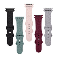 Cinq bracelets Apple Watch en silicone aux couleurs noir, vert clair, rose, rouge bordeaux et gris, textures élégantes,.