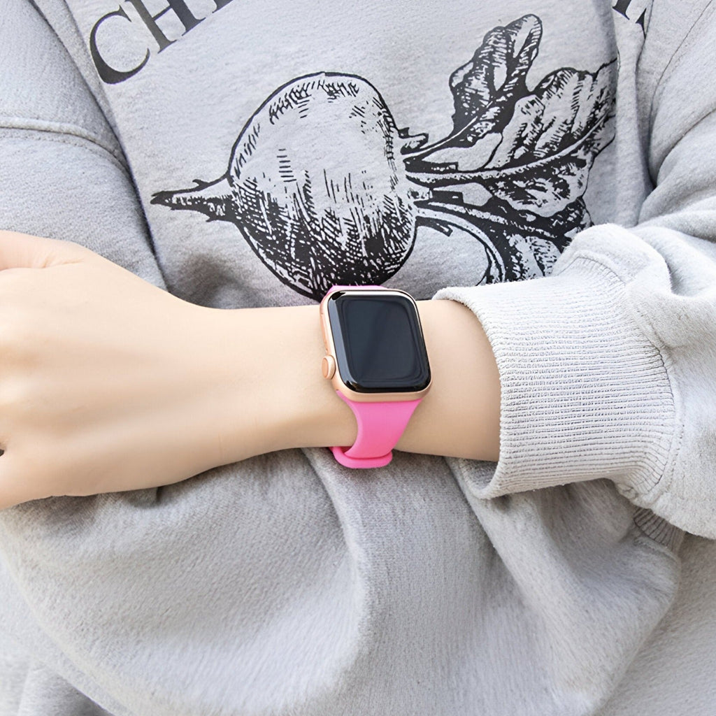 Bracelet Apple Watch en silicone rose vif porté sur poignet féminin avec sweat gris clair imprimé noir.