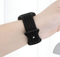 Bracelet Apple Watch en silicone noir perforé avec fermeture ajustable porté au poignet féminin.