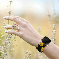 Bracelet Apple Watch en tissu élastique noir avec motif floral jaune vif, modèle Leyra, porté au poignet féminin en.
