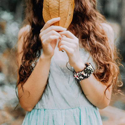 Bracelet Apple Watch élastique en tissu floral multicolore porté par femme avec robe bleue pâle.