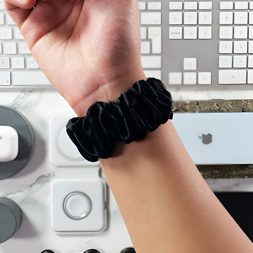 Bracelet élastique noir en tissu style scrunchie porté au poignet féminin pour Apple Watch.