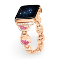 Bracelet Apple Watch or rosé avec incrustation de sable rose et détails en pierres blanches.