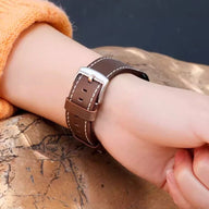 Bracelet de montre en cuir marron avec surpiqûres claires et boucle argentée porté au poignet.