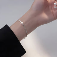 Bracelet délicat en argent sterling avec petite croix chrétienne sur chaîne fine, porté au poignet féminin.