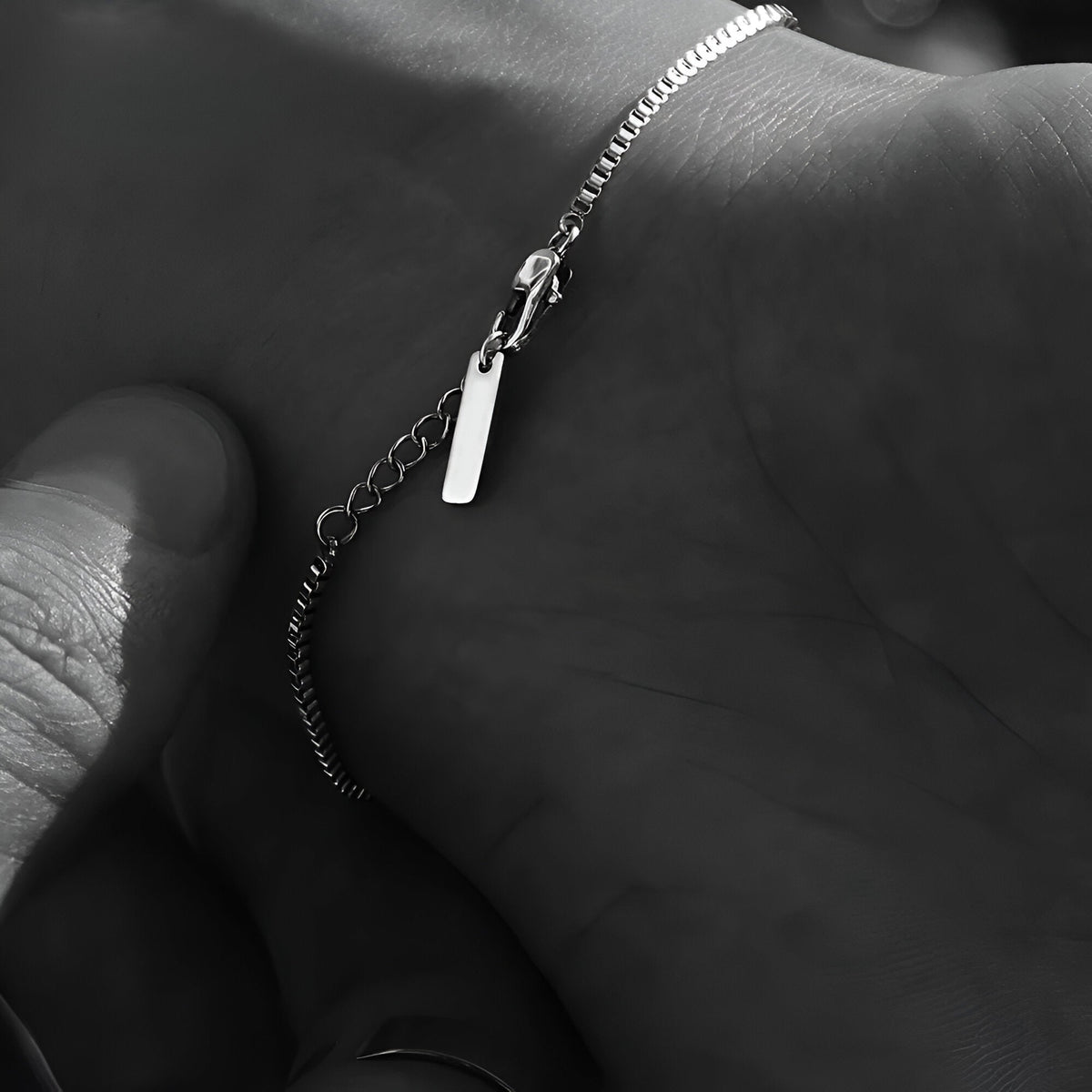 Bracelet homme fin en acier inoxydable argenté avec petite plaque rectangulaire et chaîne délicate.
