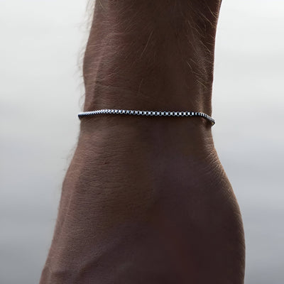 Bracelet fin en acier inoxydable argenté, maillons tressés, porté au poignet homme.