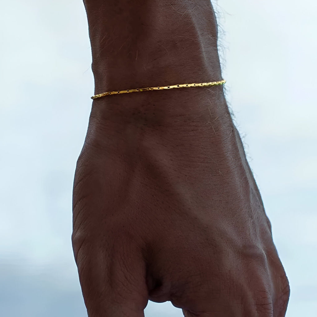 Bracelet fin en acier inoxydable doré, style torsadé, porté au poignet masculin.