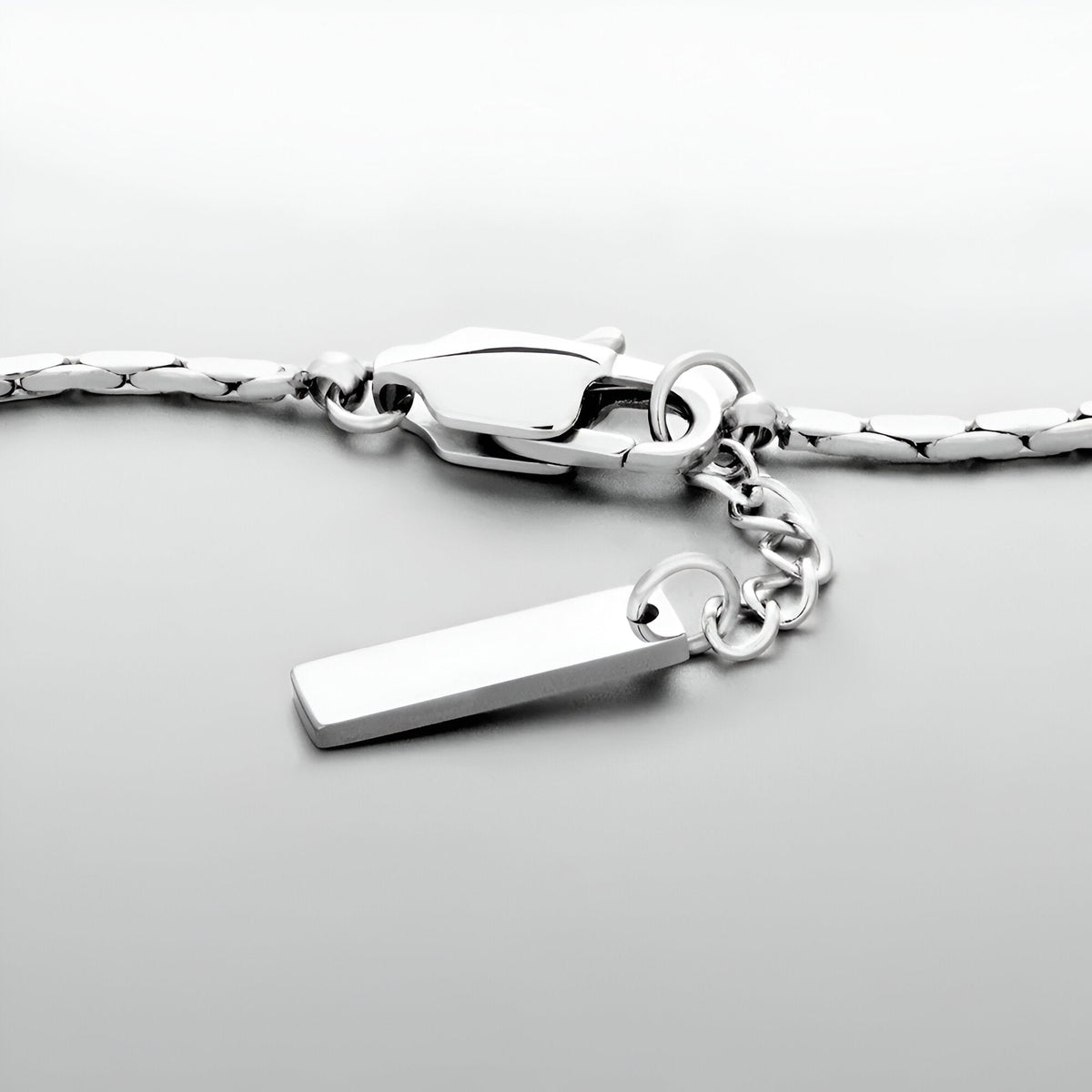 Bracelet en acier inoxydable argenté avec pendentif rectangulaire et fermoir mousqueton.