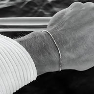 Bracelet fin doré en acier inoxydable lucide, modèle Julio, porté au poignet homme avec chemise blanche rayée.