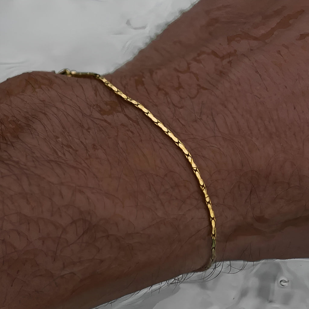 Bracelet fin en acier inoxydable doré, style minimaliste et waterproof, porté au poignet homme.